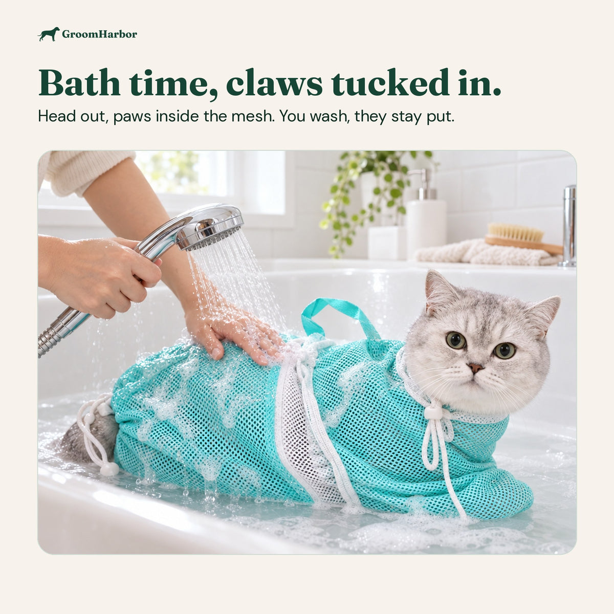 Grey cat in the turquoise mesh bath bag being rinsed with a handheld shower in a white bathtub